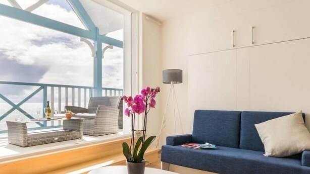 A modern living room with a blue sofa, white coffee table, and a view of the sky through a balcony. - Beachfront Apartment with Stunning Sea Views, Wi-Fi, and BBQ Area (Piriac-sur-Mer)
