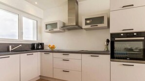 A modern kitchen with white cabinets, a black countertop, a stainless steel range hood, and a built-in oven. - Beachfront Apartment with Stunning Sea Views, Wi-Fi, and BBQ Area (Piriac-sur-Mer)