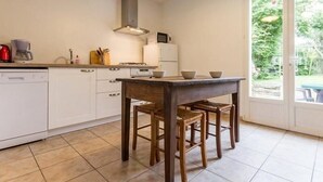A modern kitchen with white cabinets, a wooden table, and a view of the garden through the door.