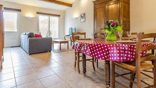 A dining area with a table set for four, wooden chairs, and a vase with flowers.
