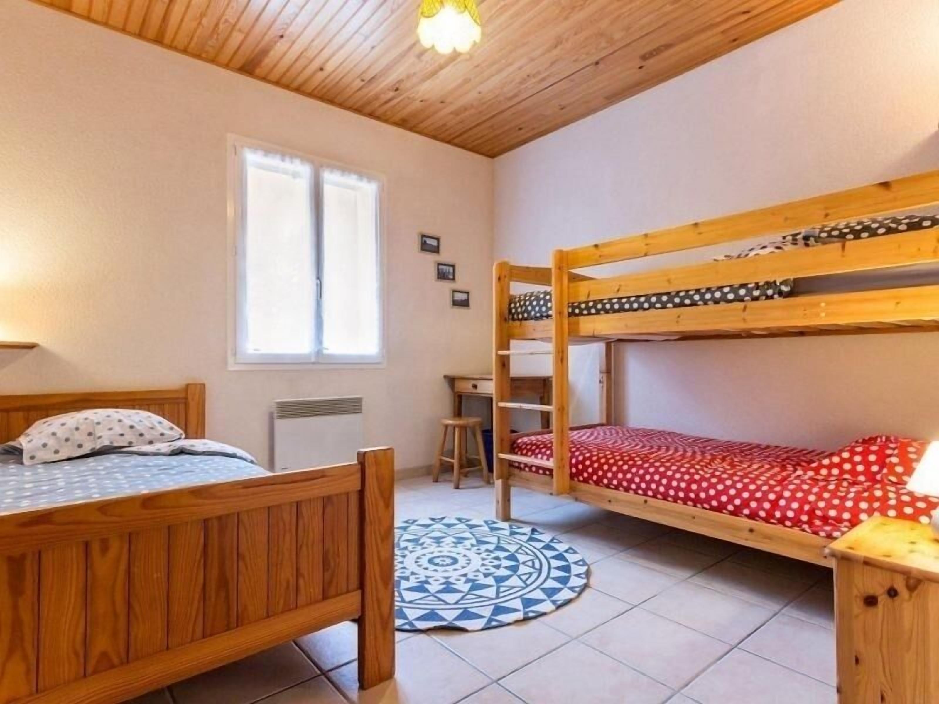A room with two wooden bunk beds, a single bed, a desk, and a patterned rug.