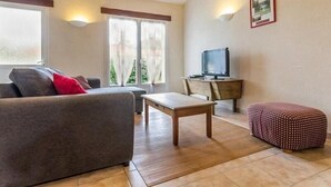 A cozy living room with a sofa, a small table, a television on a wooden stand, and a window with curtains.