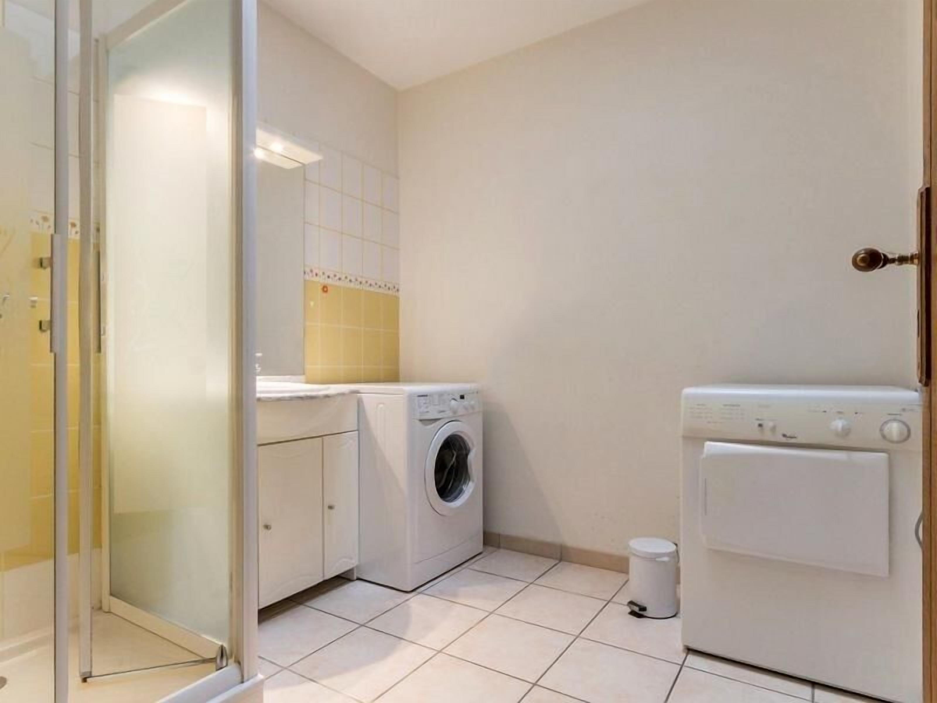 A compact laundry room with a washing machine, dryer, and a trash bin.