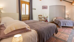 Un dormitorio acogedor con dos camas, techo de madera, una ventana con cortinas, una silla y un florero con flores.