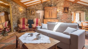 Una habitación acogedora con pared de piedra, vigas de madera, un sofá, dos sillones, una mesa con tetera y un candelabro.
