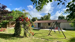 A backyard with a swing set, a covered seating area, and a house with a tiled roof. - Countryside Retreat: Cozy 3-Bed Gîte with Garden, Terrace & Petanque near Pornic (Frossay)