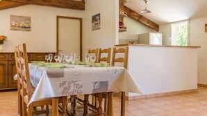 A dining area with a table set for six, wooden chairs, a white tablecloth, and a kitchen in the background. - Countryside Retreat: Cozy 3-Bed Gîte with Garden, Terrace & Petanque near Pornic (Frossay)