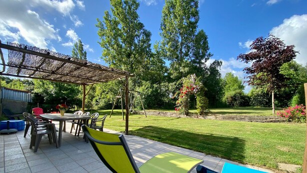 An outdoor patio with a table and chairs, a swing set, and a garden area with trees and a lawn. - Countryside Retreat: Cozy 3-Bed Gîte with Garden, Terrace & Petanque near Pornic (Frossay)