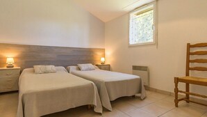 A bedroom with two single beds, a wooden chair, a nightstand with a lamp, and a window with blinds. - Countryside Retreat: Cozy 3-Bed Gîte with Garden, Terrace & Petanque near Pornic (Frossay)