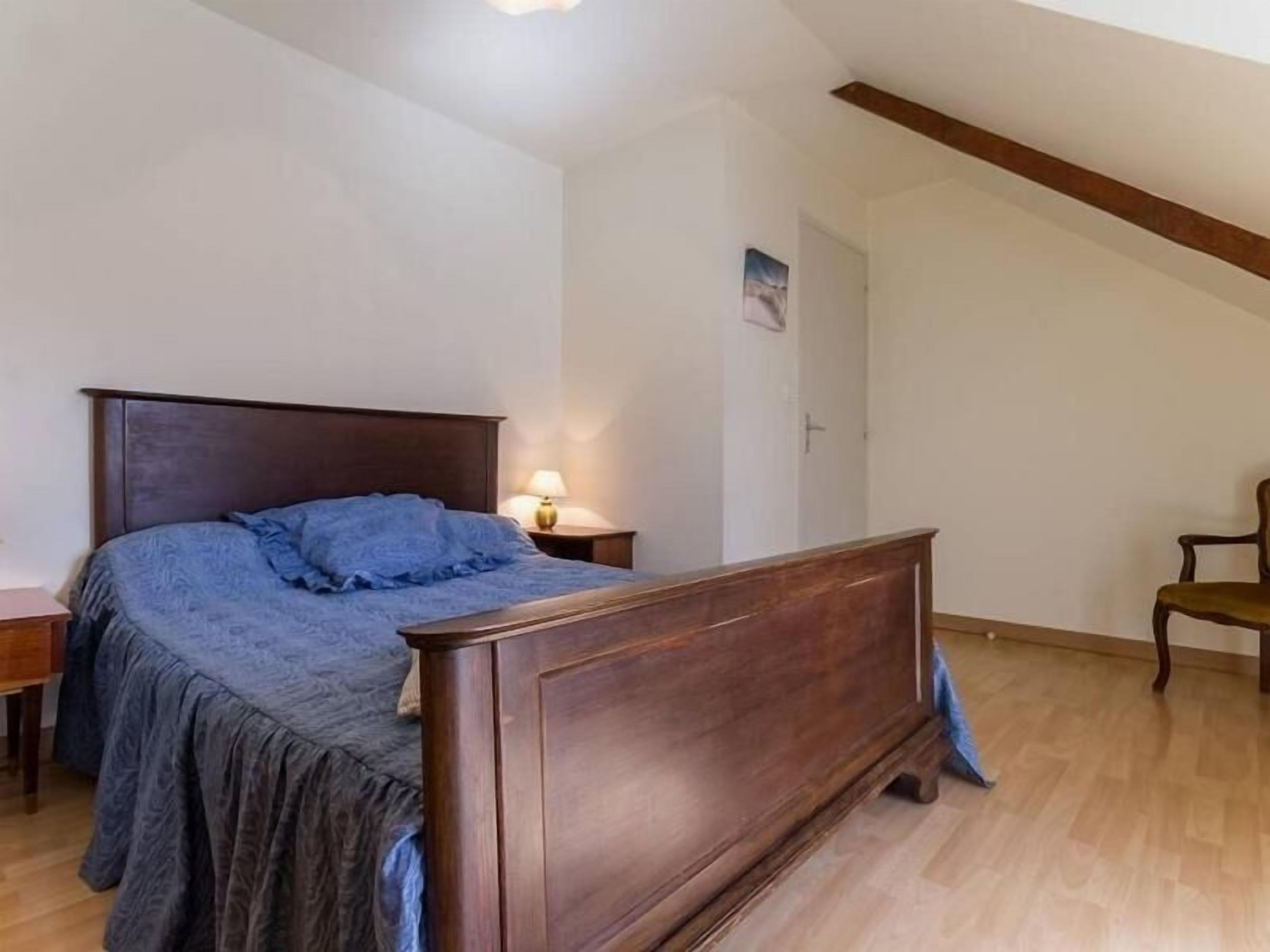 Ein Schlafzimmer mit einem hölzernen Bett, einem Nachttisch, einer Lampe und einem Sessel.