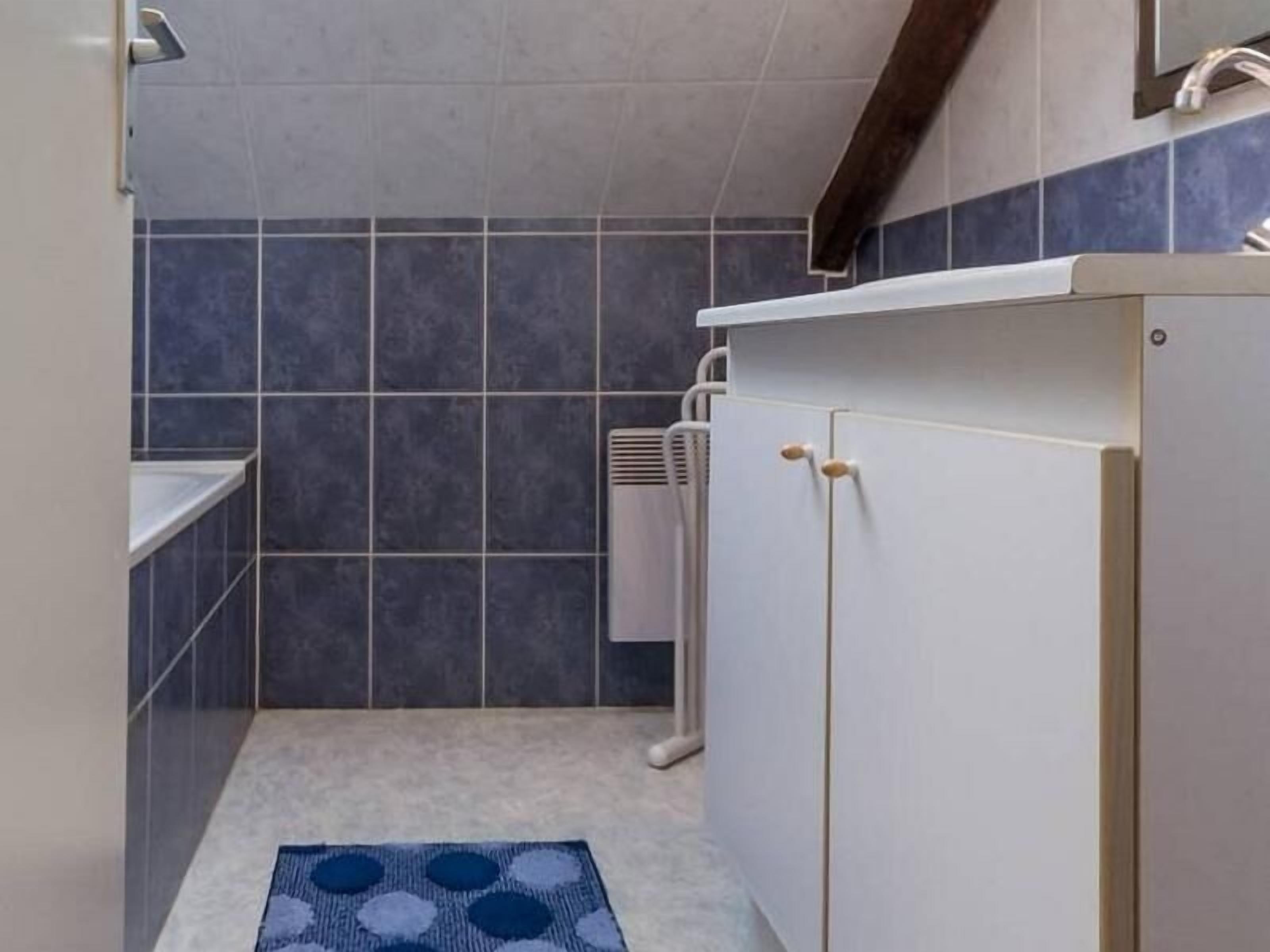 Een badkamer met donkerblauwe tegels, een wit kastje met houten handgrepen en een wit aanrecht.