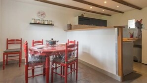 Un coin repas avec une table ronde, six chaises rouges, un espace cuisine doté d’un plan de travail et une étagère avec des bocaux.
