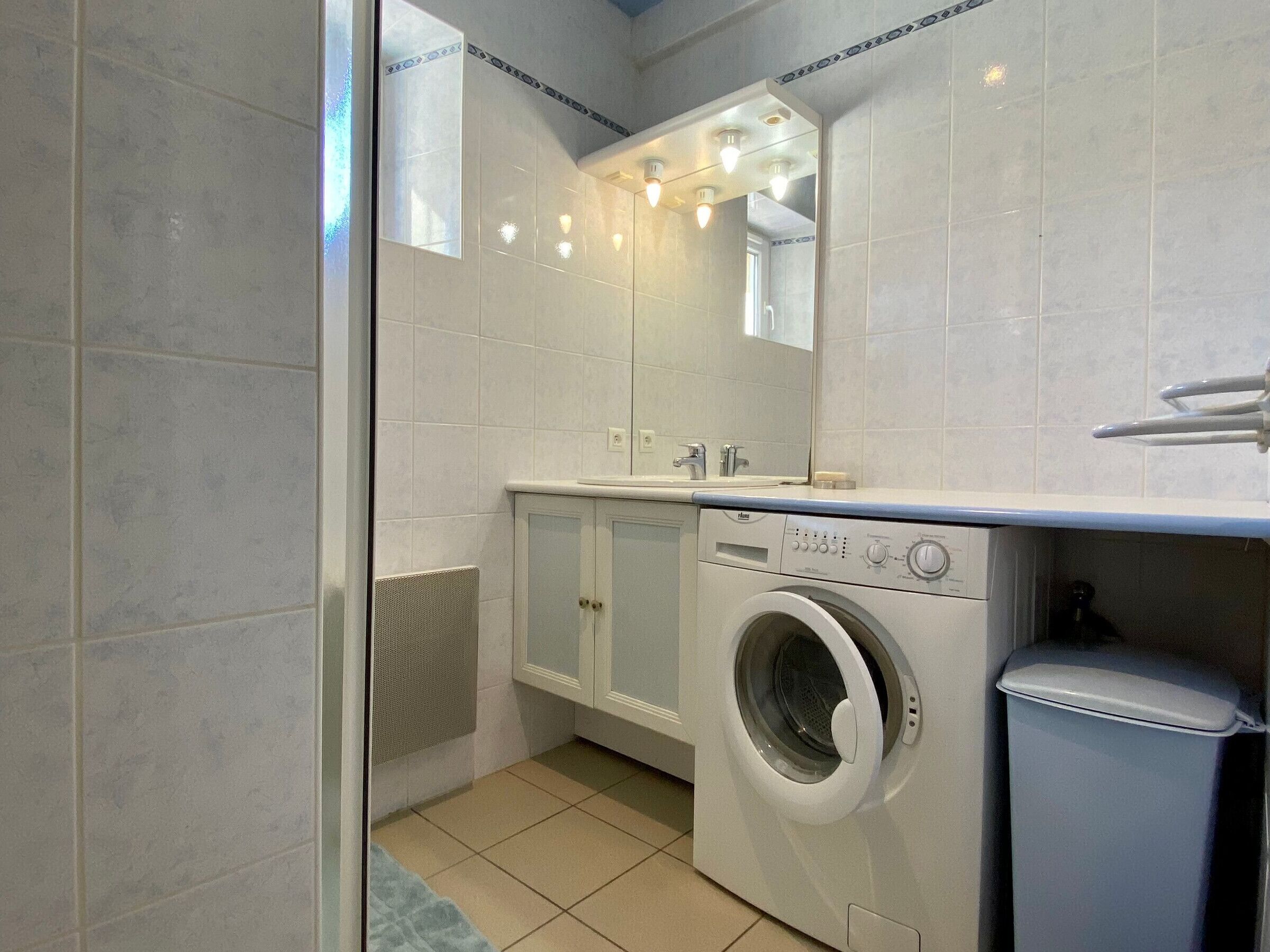 A compact, modern bathroom with a washing machine, a sink, and a mirror.