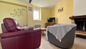 Een woonkamer met een rode leren bank, een grijze fauteuil, een televisie op een houten kast en een open haard.