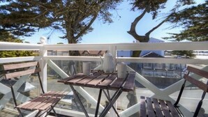 A glass-enclosed balcony with wooden benches and a table, overlooking a residential area with trees and houses. - Luxury Seaside Gîte with Balcony, Parking, and Baby Equipment (Saint-Michel-Chef-Chef)