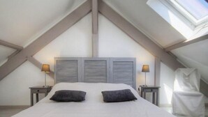 A bedroom with a sloped ceiling, a bed with two pillows, two bedside lamps, and a window. - Luxury Seaside Gîte with Balcony, Parking, and Baby Equipment (Saint-Michel-Chef-Chef)