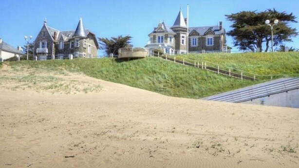 A coastal property with a sandy beach, a staircase leading to a house, and a clear blue sky. - Luxury Seaside Gîte with Balcony, Parking, and Baby Equipment (Saint-Michel-Chef-Chef)