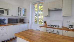 A kitchen with white cabinets, a wooden countertop, a gas stove, a microwave, and a window with blinds. - Luxury Seaside Gîte with Balcony, Parking, and Baby Equipment (Saint-Michel-Chef-Chef)