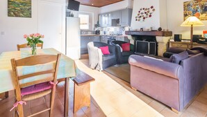 Ein geräumiges Wohnzimmer mit Esstisch, Stühlen und einer Couch. Im Hintergrund ist eine Küche mit modernen Geräten und einer gefliesten Spritzschutzwand zu sehen.