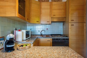 Une cuisine avec des meubles en bois, un plan de travail en granit, un four à micro-ondes, un évier, une cuisinière et une machine à café.