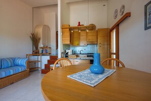 Un salon avec un canapé, une table à manger ornée d’un vase, et une cuisine en arrière-plan.