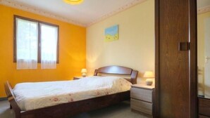 A bedroom with a bed, bedside tables, a wooden wardrobe, and a window with curtains. - Charming Cottage with Garden near Nantes & Vannes – Pet-Friendly (La Chapelle-Launay)