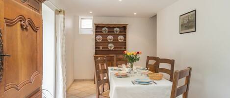Un comedor con un armario de madera, una mesa de comedor preparada para cuatro personas y un escurreplatos de pared.