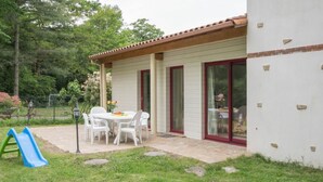 Un patio con tavolo e sedie, uno scivolo blu e una casa con una porta rossa e finestre.