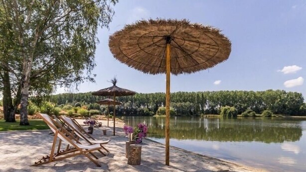 Un cadre paisible au bord du lac, avec des chaises longues et un parasol en chaume.