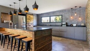 Une cuisine moderne dotée d’un îlot central, de tabourets de bar, de luminaires suspendus et d’un mur d’accent en pierre.