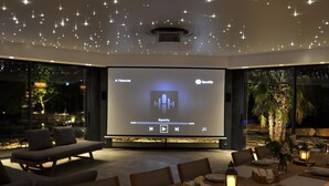 Un espace de restauration extérieur moderne, doté d’un grand écran diffusant Spotify, entouré de sièges confortables et créant une ambiance chaleureuse.