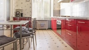 Uma cozinha compacta com armários vermelhos, uma mesa de jantar com cadeiras e um radiador.