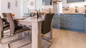 Eine moderne Küche mit blauen Schränken, einer Edelstahl-Dunstabzugshaube und einem Essbereich mit Holztisch und -stühlen.