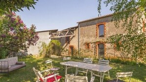 An outdoor patio with a table and chairs, surrounded by a grassy area and a stone building with windows and a staircase. - Charming Cottage in Vineyards - Near Nantes & Clisson - WiFi, Family-Friendly (Monnières)