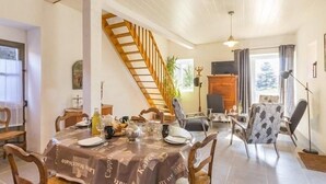 A dining area with a wooden staircase, a dining table set with plates, glasses, and a bottle, and a view of the outdoors through a window. - Charming Cottage in Vineyards - Near Nantes & Clisson - WiFi, Family-Friendly (Monnières)