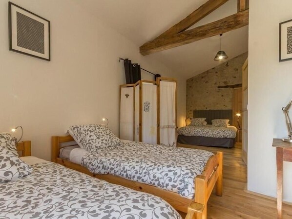 A bedroom with two single beds, a wooden wardrobe, and a small desk with a lamp.