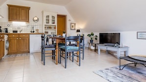 Een kleine keuken met houten kastjes, een zithoek met een tafel en stoelen, een televisie en een bijzettafeltje.