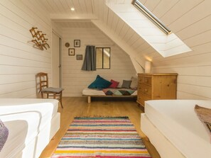 Ett mysigt sovrum på vinden med ett sluttande tak, en byrå i trä, en säng med färgglada kuddar, en stol och en randig matta.