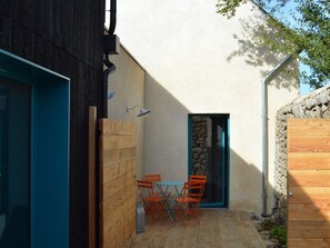 Une terrasse en bois avec une table et des chaises, un mur en pierre et une porte bleue.