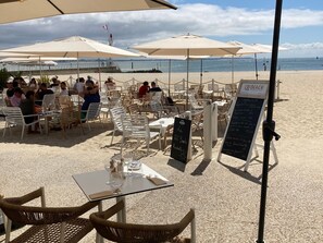 Ein Café direkt am Strand mit Außenbereich, Tischen und Sonnenschirmen.
