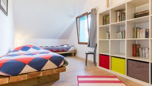 Un dormitorio con cama tipo loft, una estantería y un ventanal con cortinas.