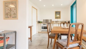 Un comedor con una mesa y sillas de madera, una cocina al fondo y un cuadro en la pared.