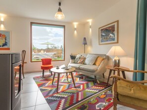 A living room with a sofa, a coffee table, a red chair, a patterned rug, and a large window with a view of the outdoors. - Wooden House between Land and Sea in Guérande (Guérande)