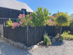 A building with a dark wooden fence, a gravel driveway, and a tree with pink flowers. - Wooden House between Land and Sea in Guérande (Guérande)