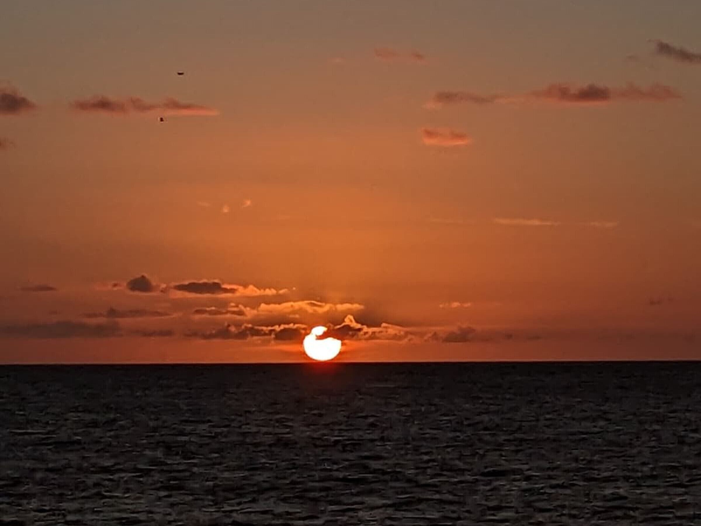 Ein Sonnenuntergang über einem ruhigen Meer mit klarem Horizont.