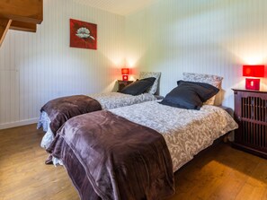 Habitación con dos camas, suelo de madera, un cuadro de flores rojas y dos lámparas rojas sobre mesitas de noche.