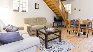A spacious living room with a high wooden staircase, a sofa, a coffee table, and a dining area with chairs and a table. - "Charming Gîte in Brière Park, 15km from La Baule Beach" (Saint-Lyphard)