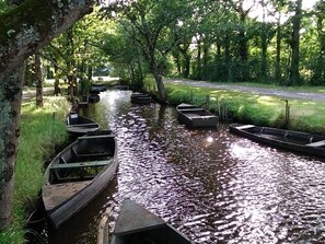 A narrow waterway lined with boats, surrounded by trees and grassy banks.
