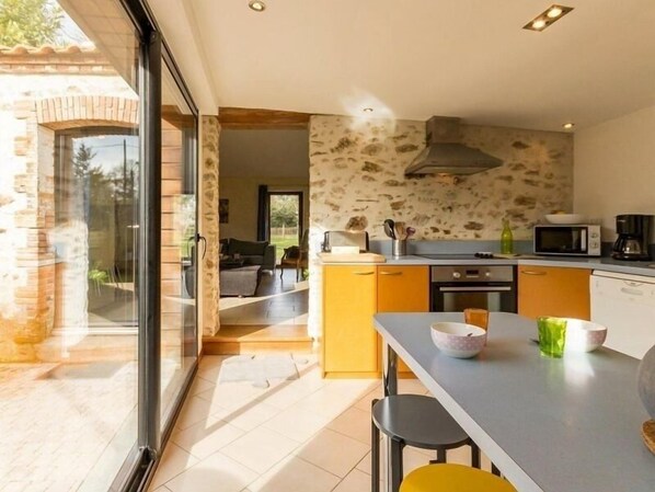 A modern kitchen with a stone backsplash, a dining area with a table and chairs, and a view of the outdoor patio.