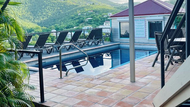 Zona de piscina con sillones de descanso, una piscina y vistas a una ladera verde.